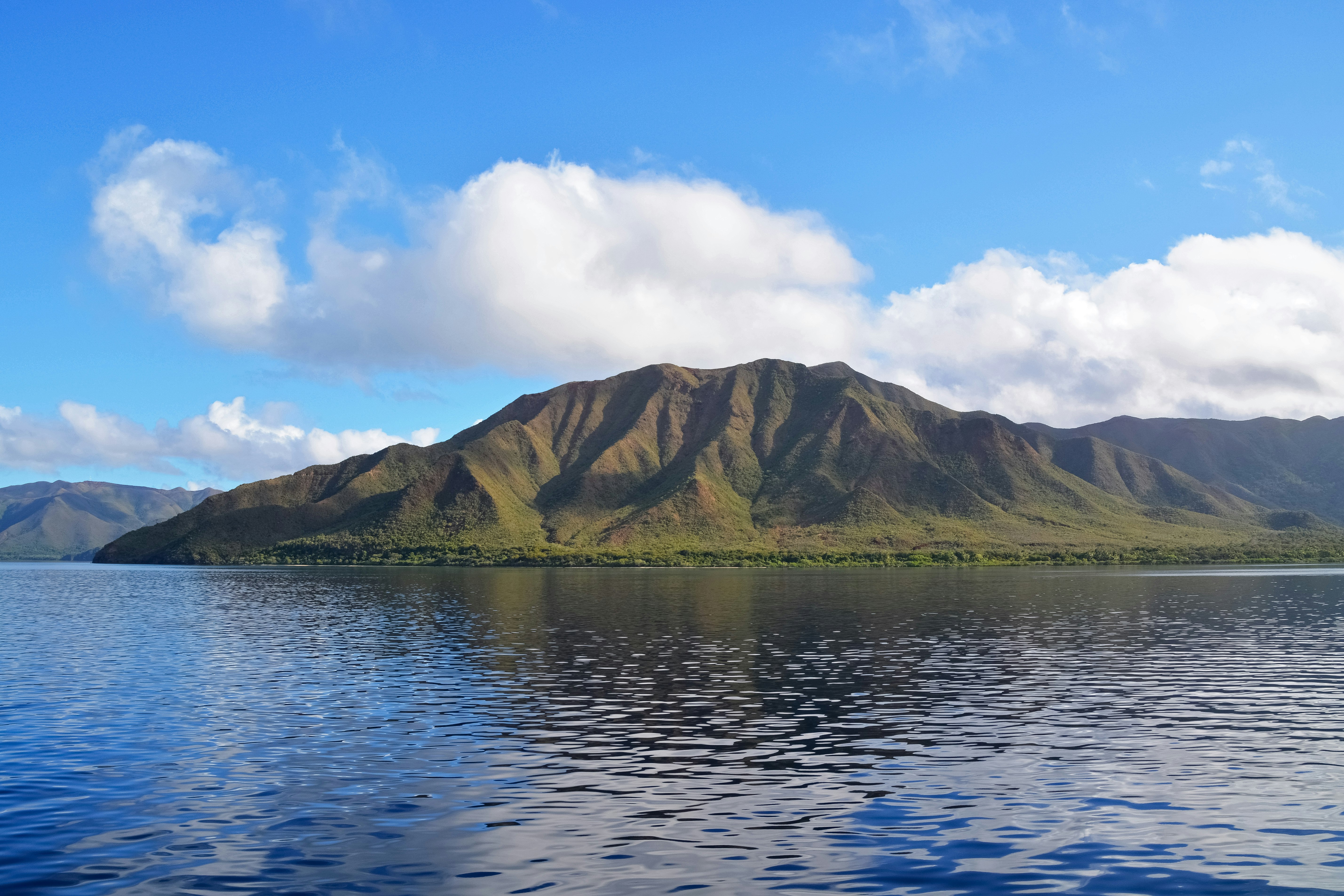 brown mountain beside body of water under blue sky during daytime